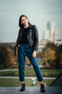 Девушка в кожаной куртке и синих джинсах позирует на фоне городского вида