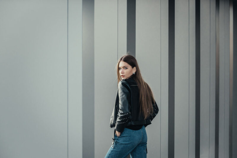 Городской портрет девушки, смотрящей в камеру на фоне серого фасада здания