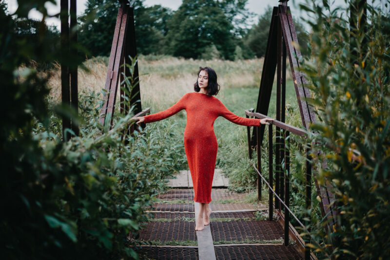 девушка в красном платье на железном мостике над небольшой рекой