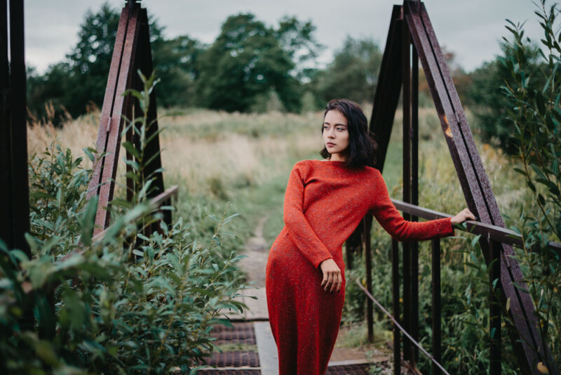 девушка в красном платье на железном мостике над небольшой рекой