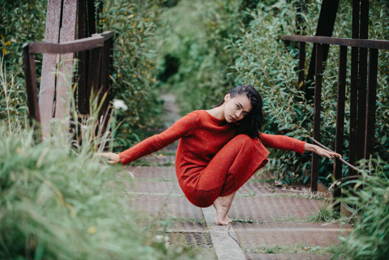 портрет девушки в красном платье сидя на корточках на железном мостике