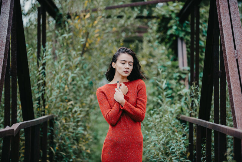 девушка в красном платье на фоне тёмной зелени начала осени