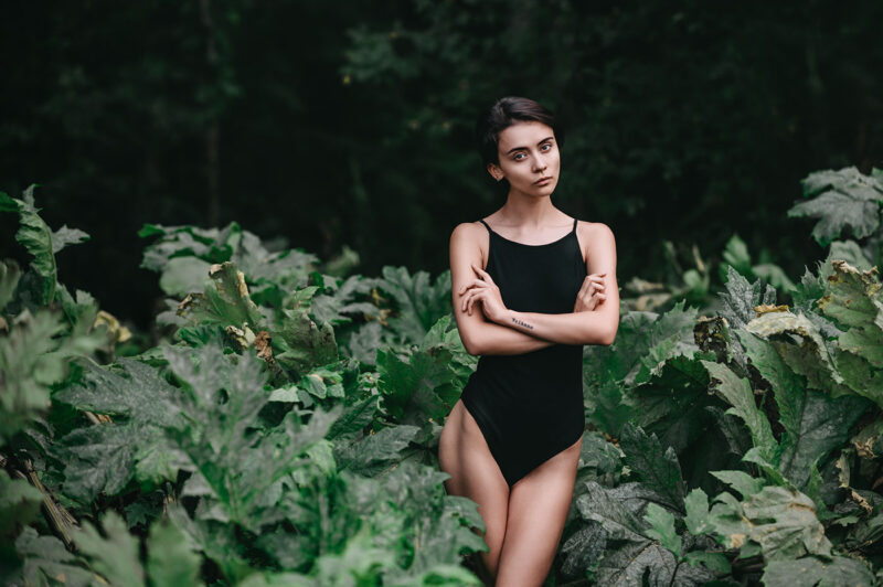 Портрет в лесу полуобнажённой девушки среди крупных листьев борщевика