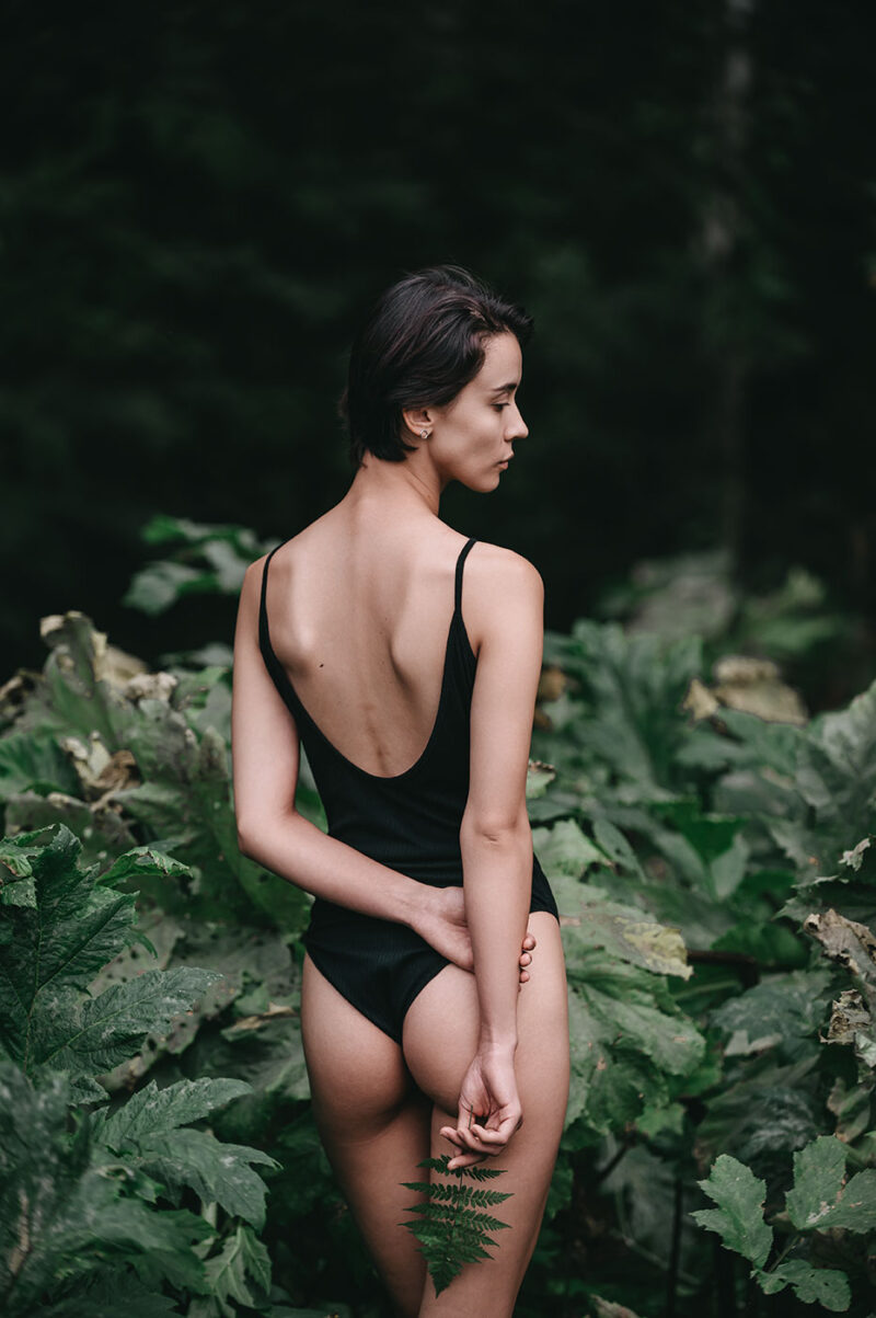 Девушка в боди с папоротником в руке среди листьев борщевика