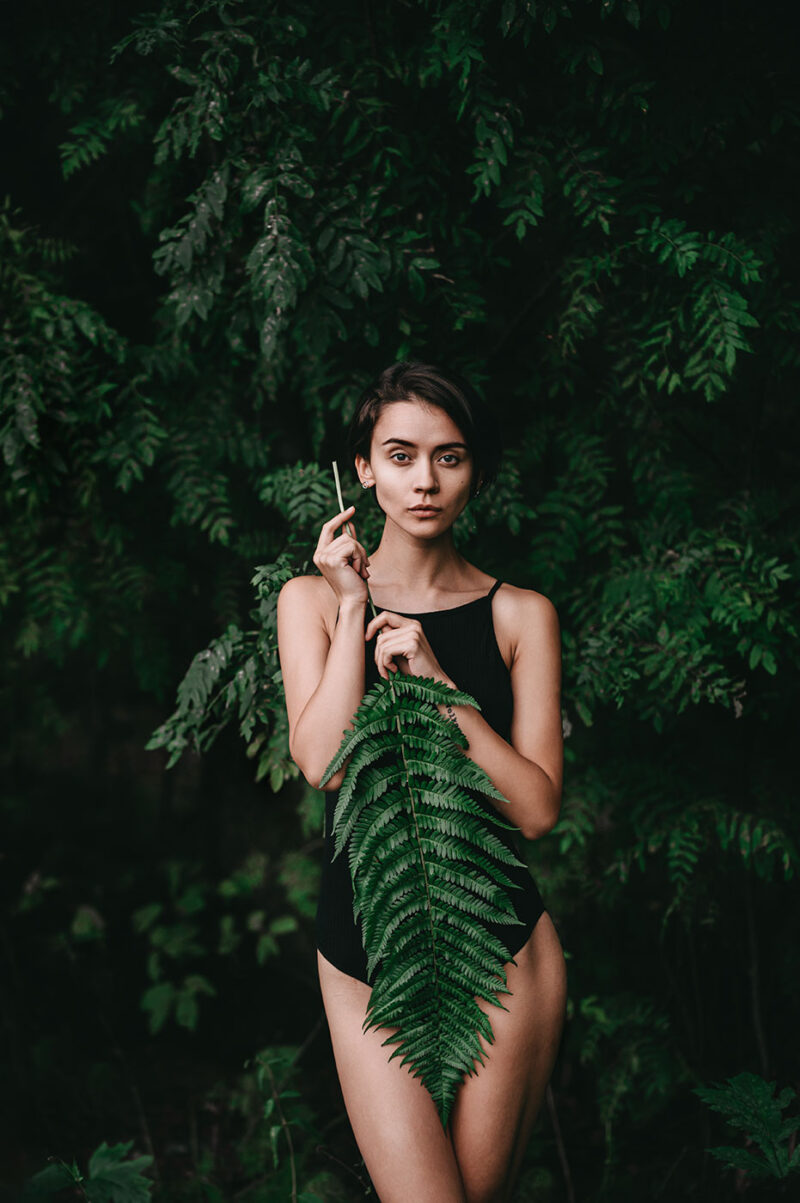 Девушка в боди с папоротником на фоне тёмного леса