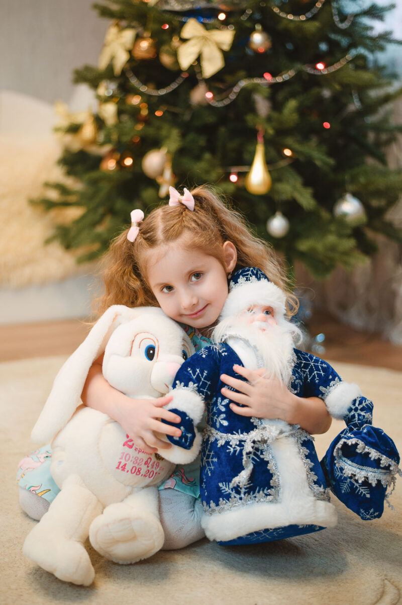 Девочка на ковре с игрушками на фоне украшенной ёлки, домашняя съёмка