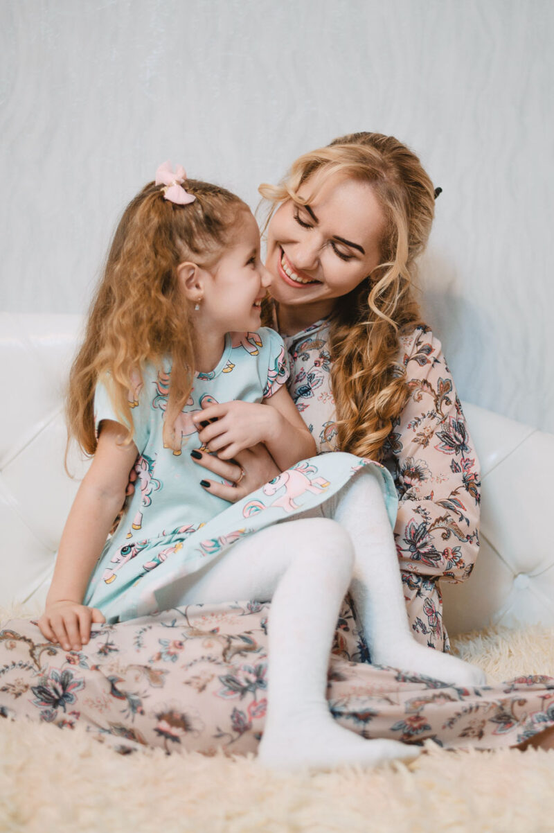 Мама и дочка улыбаются друг другу, сидя на кровати в спальне