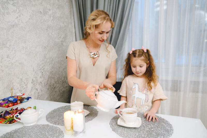 Мама наливает чай рядом с дочкой за кухонным столом