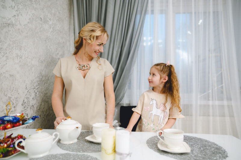Мама смотрит на дочку у окна во время домашнего чаепития