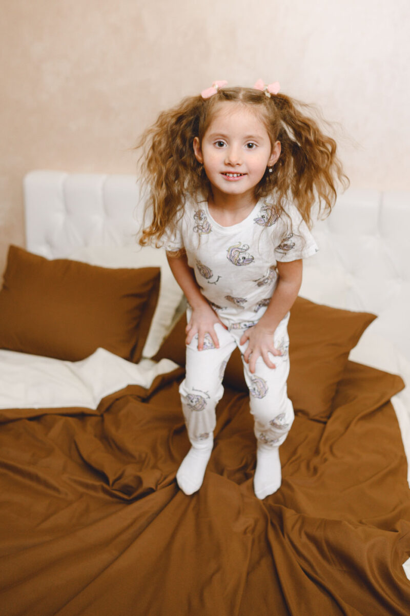 Девочка в пижаме прыгает на кровати в светлой спальне во время семейной съёмки