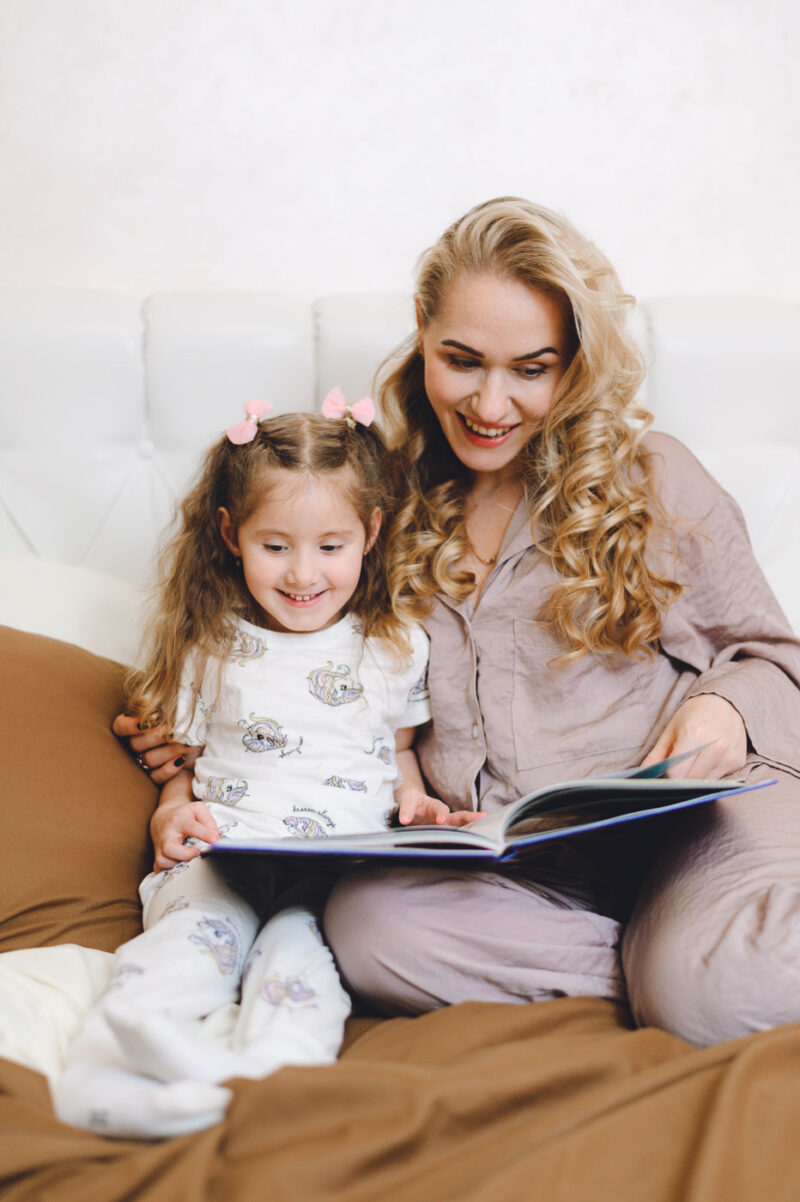 Мама с дочкой рассматривают книгу, сидя в уютной спальне