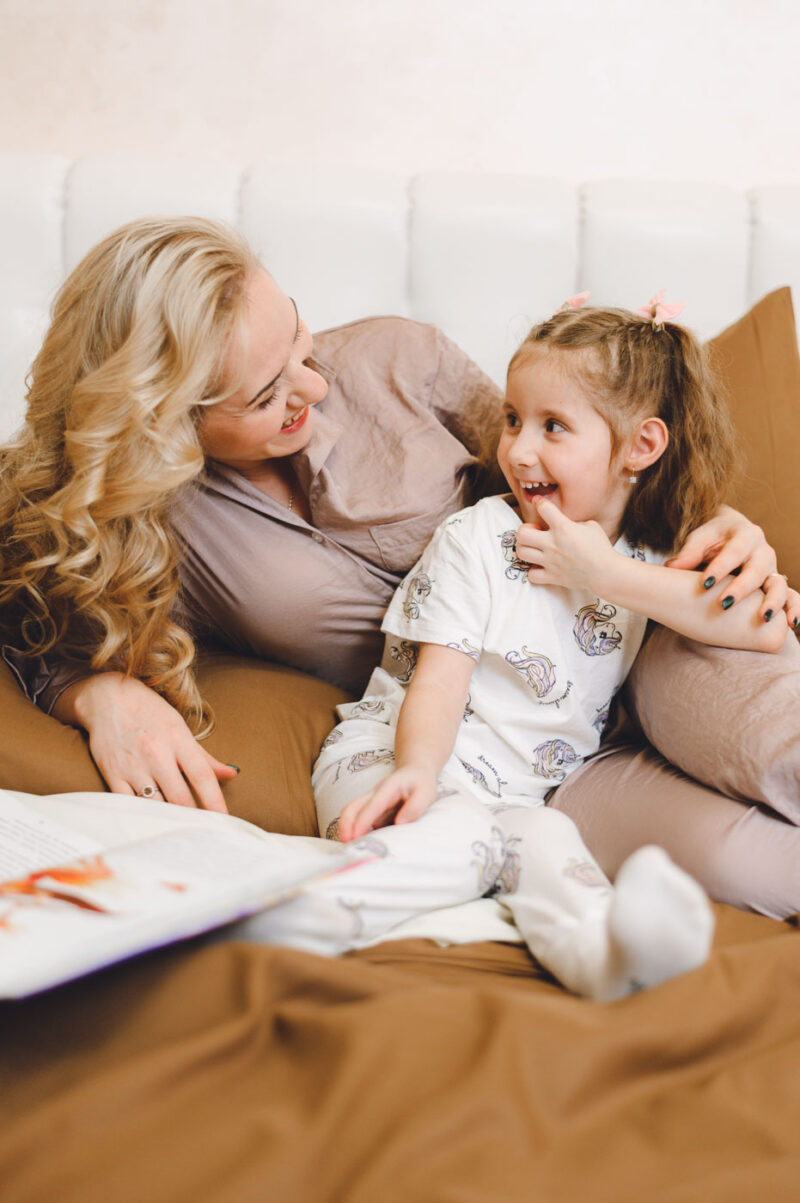 Мама и дочка смеются на кровати в домашнем интерьере