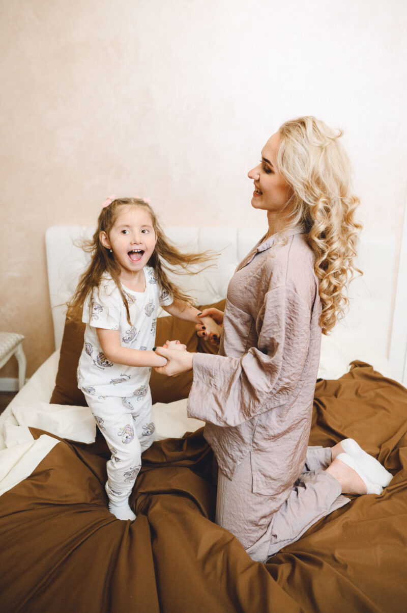 Мама и дочка играют на кровати во время домашней фотосессии