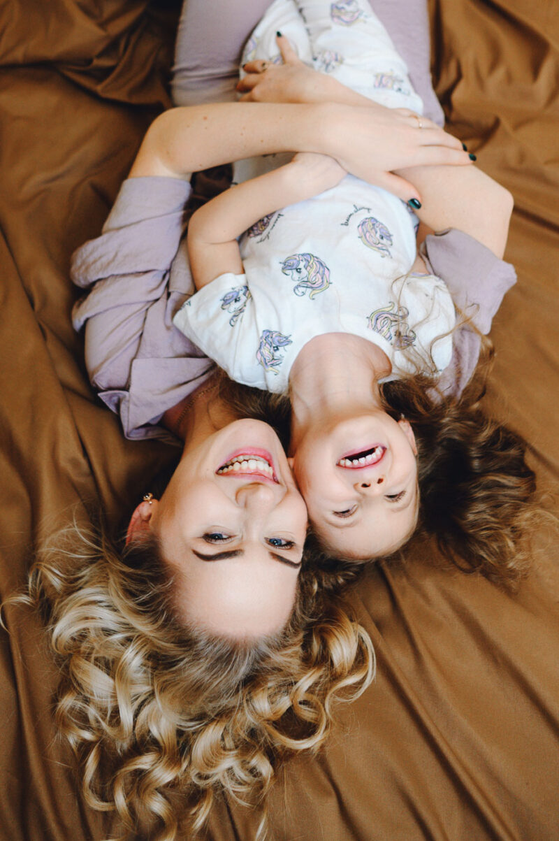 Вид сверху - мама и дочка лежат на кровати и смеются