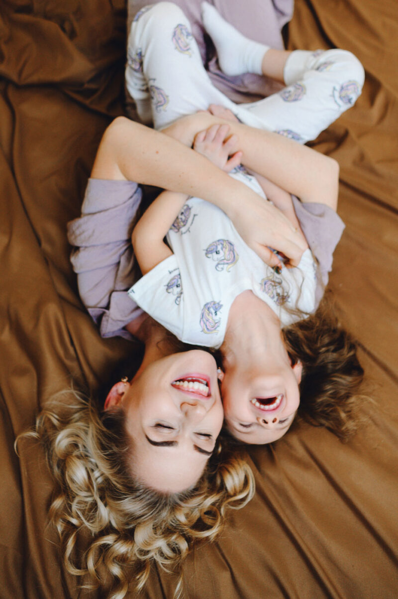 Фотосессия мамы с дочкой дома - весёлые объятия на кровати во время игры