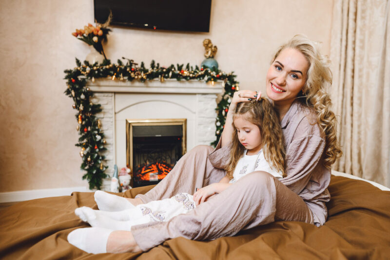 Мама обнимает дочку на кровати на фоне рождественского декора