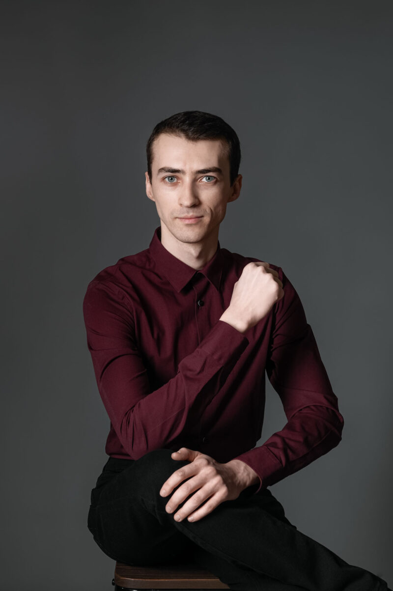 Мужчина в бордовой рубашке сидит на стуле в студии