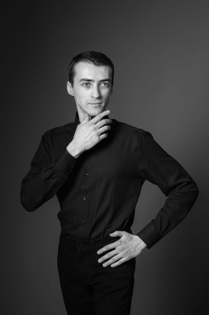 Мужчина стоит вполоборота, поднеся руку к лицу, студийный свет