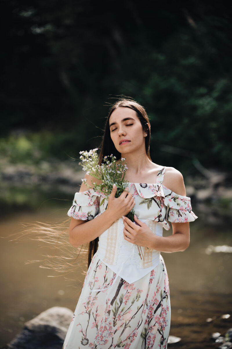 портрет девушки с букетом полевых цветов в лёгком летнем платье на природе на фоне лесной реки