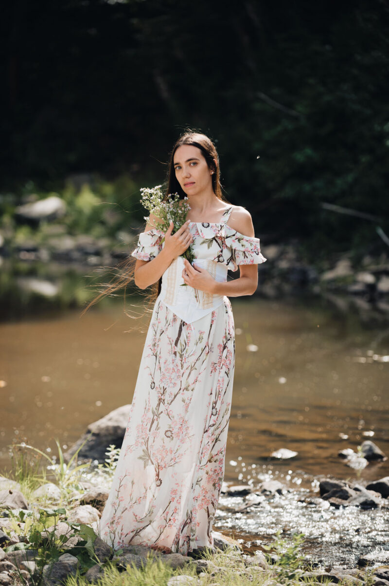 портрет девушки с букетом полевых цветов в лёгком летнем платье на природе на фоне лесной реки