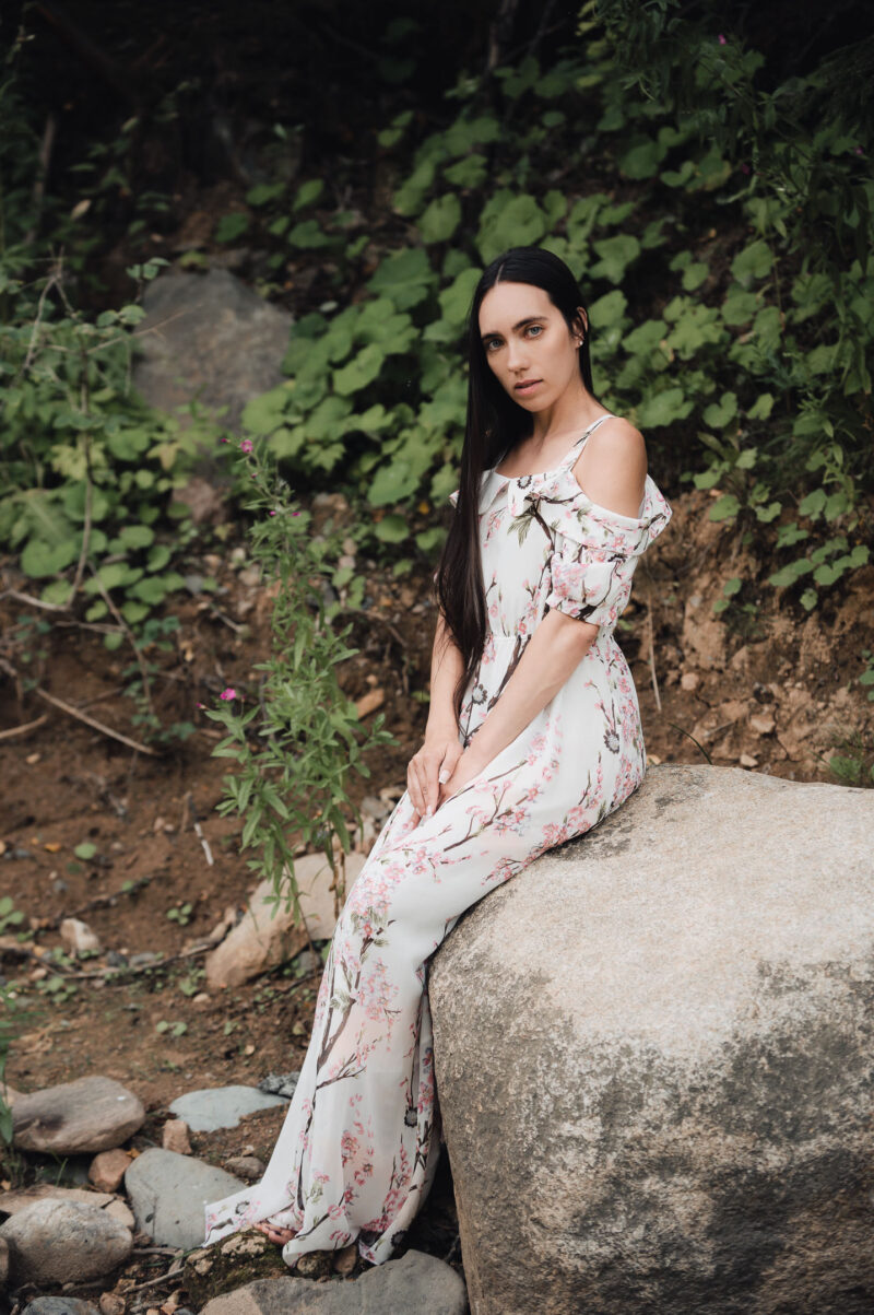 портрет девушки на природе в лёгком летнем платье, сидящей на камне