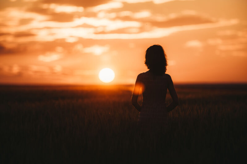 Силуэт девушки на фоне большого солнечного диска в период золотого часа