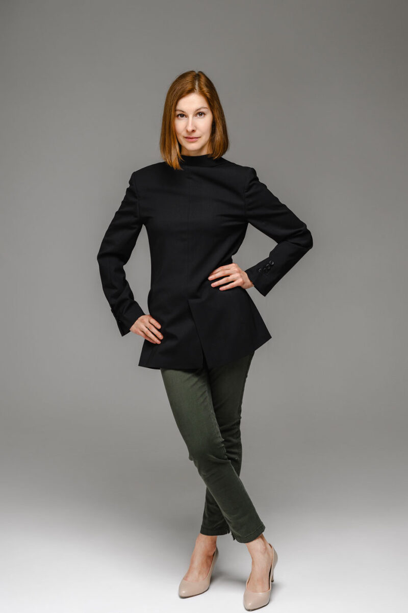 Женский портрет в полный рост в черном пиджаке и темных брюках на светлом сером фоне