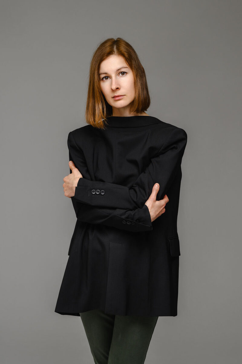 Поясной портрет девушки в объемном черном пиджаке, одетом задом наперёд