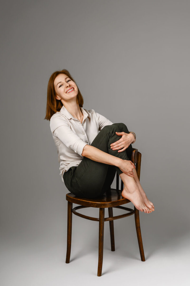 Студийный портрет девушки, сидящей на стуле, обхватив колени руками и улыбаясь