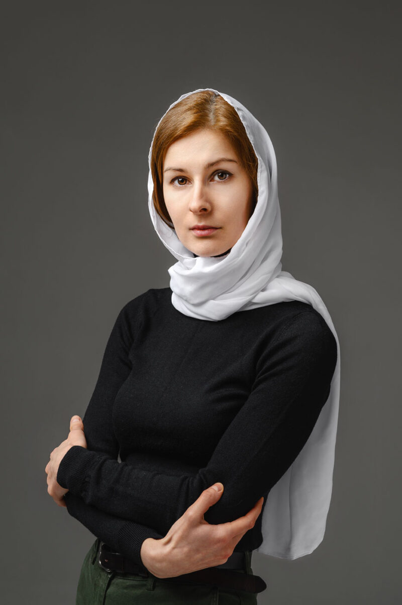 Женский портрет в черной водолазке и белом платке на голове на минималистичном темно-сером фоне