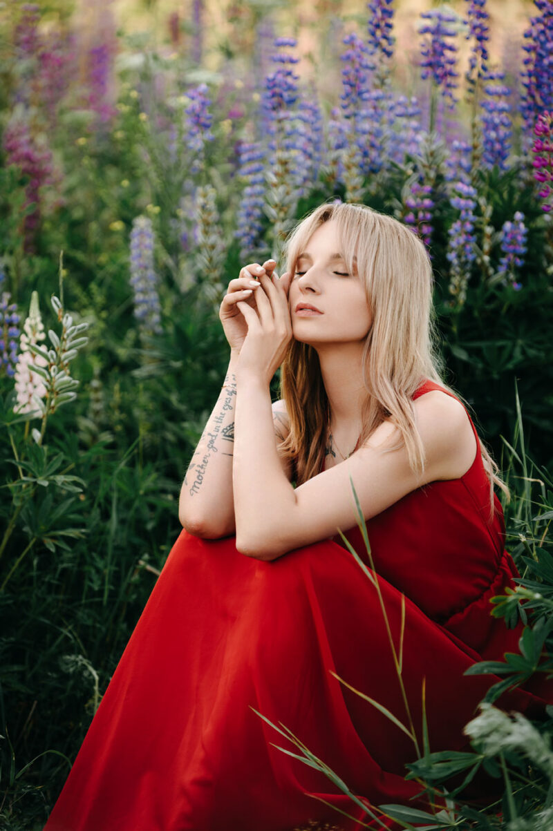 Девушка в красном платье задумчиво сидит в люпинах