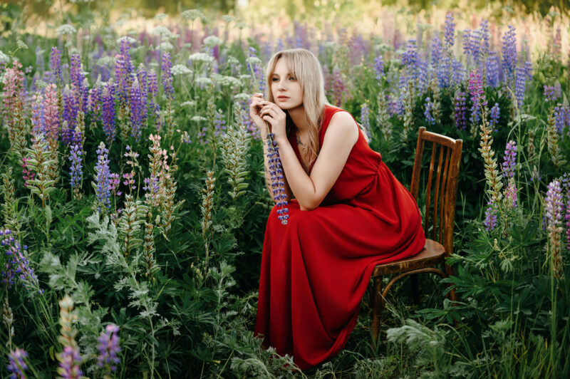 Сидящая на стуле девушка на поляне люпинов в лучах уходящего солнца