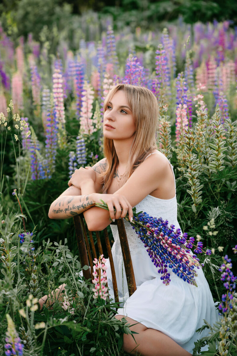 Девушка с букетом на стуле среди цветов во время индивидуальной фотосессии