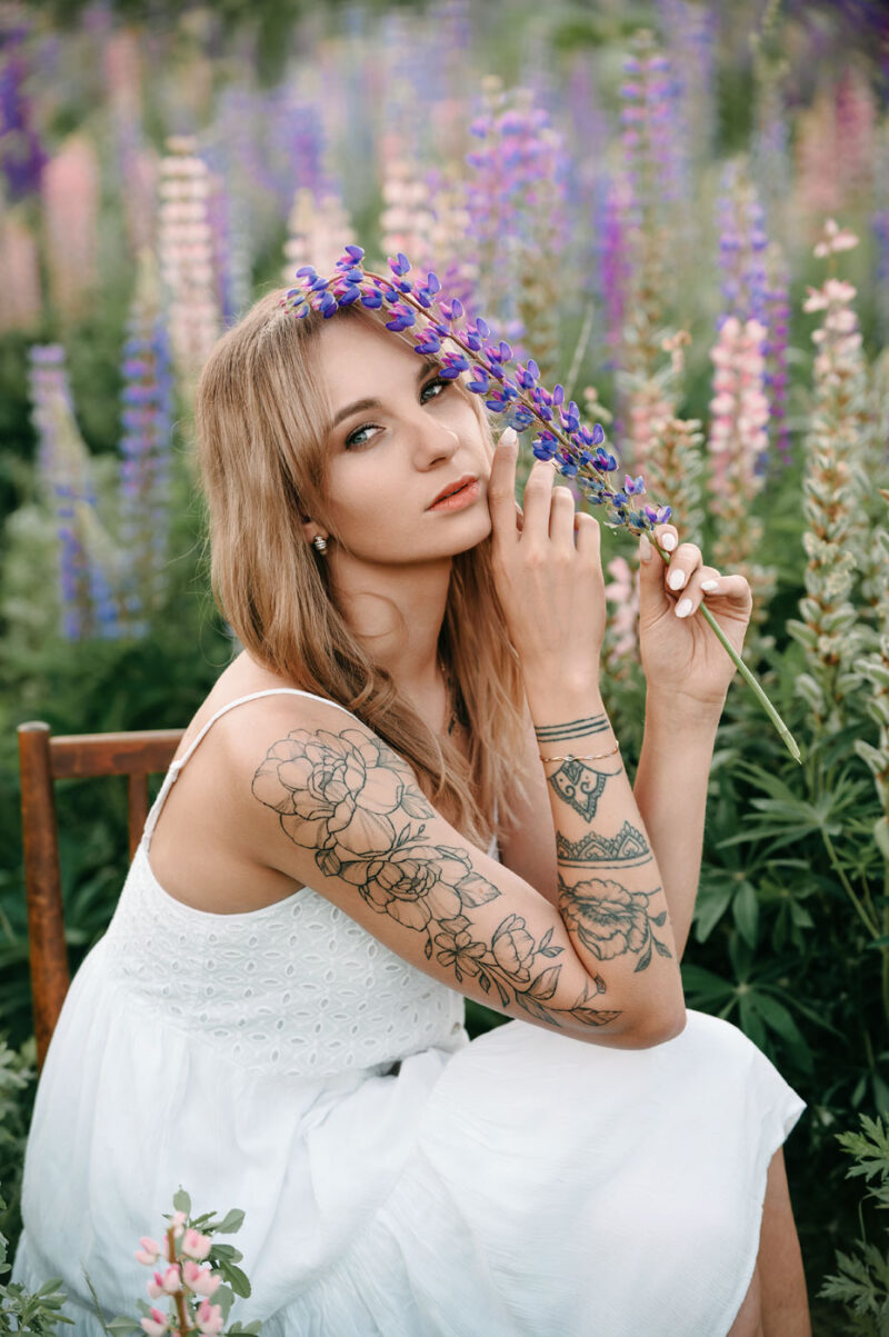 Портрет девушки в белом платье, сидящей на стуле посреди люпинового поля