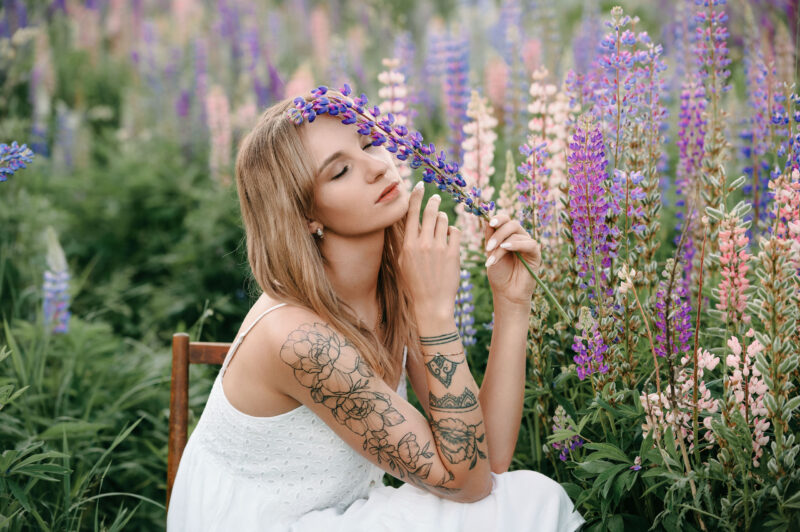 Девушка с закрытыми глазами сидит на стуле в окружении цветов люпинов