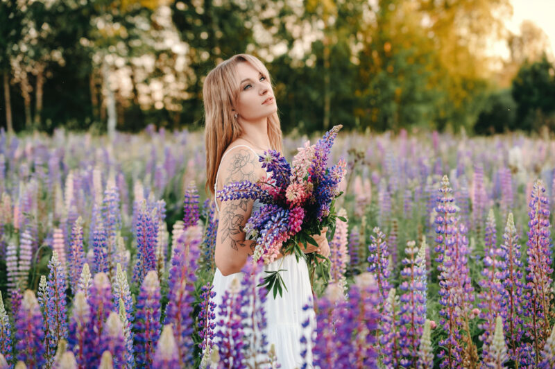 Девушка с букетом стоит на поляне люпинов в рассеянном вечернем свете