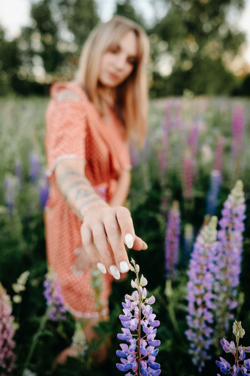 Девушка тянется рукой к цветку люпина