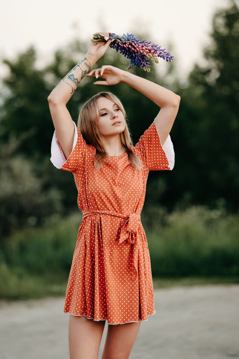 Девушка держит букет люпинов над головой, стоя на фоне деревьев