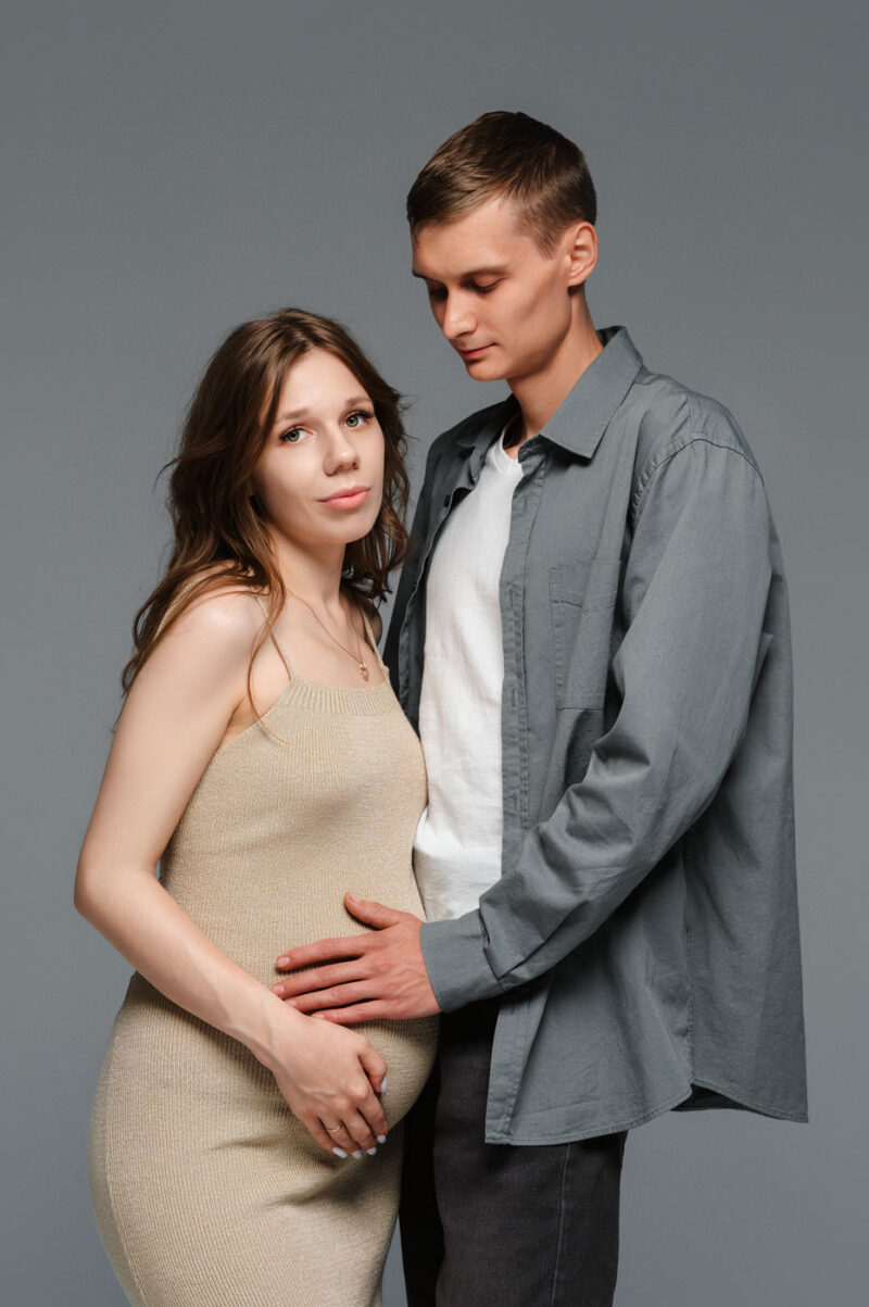 муж нежно обнимает беременную жену на студийной фотосессии
