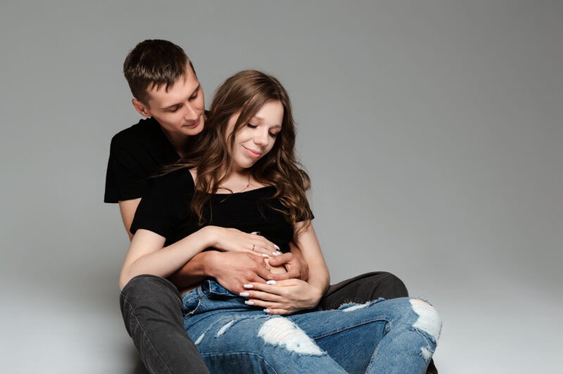 муж с беременной женой, студийный портрет сидя на полу