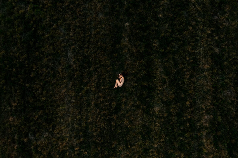Обнажённая фигура лежащей девушки, снятая с дрона на чёрном поле в Ярославле