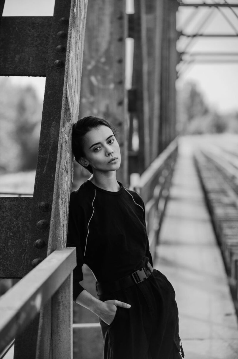 Чёрно-белый портреть девушки у грубых конструкций железнодорожного моста