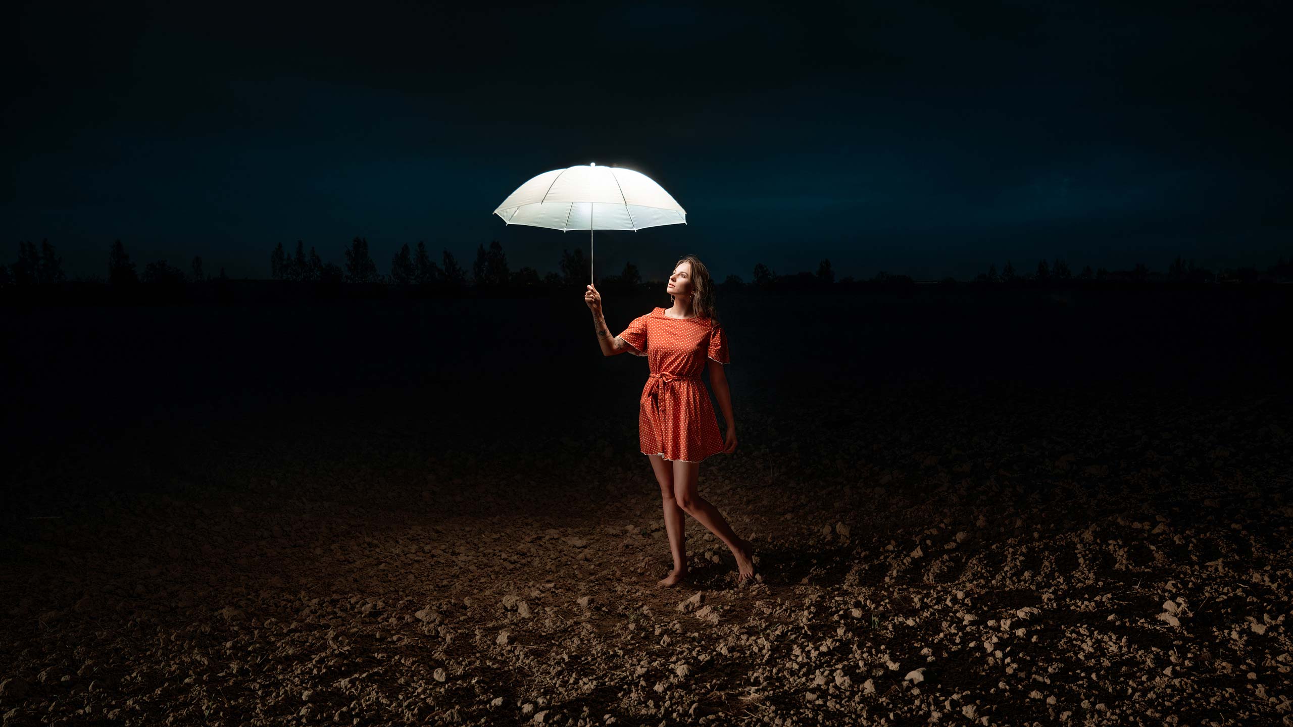 Девушка со светящимся зонтом в красном платье посреди ночного безжизненного поля